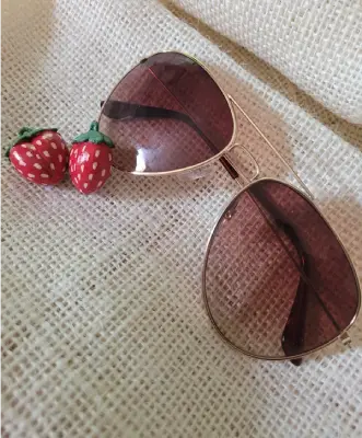 Sunglasses on a blanket with the strawberry charms hanging off them arranged in the foreground.