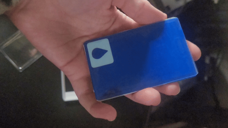 My hand flipping the keycard over so you can see there's the light blue droplet against the dark blue background on both sides.